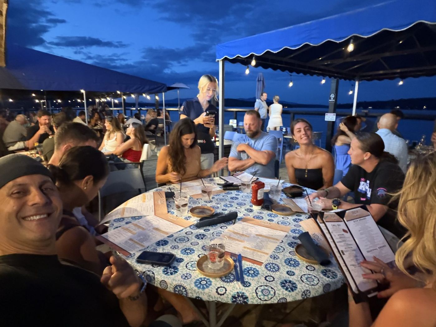 Friends around a table on a lakeside deck at dusk on Paugus Bay
