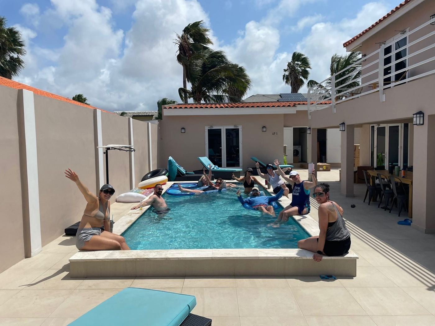 A group of friends waving from a villa pool in Aruba